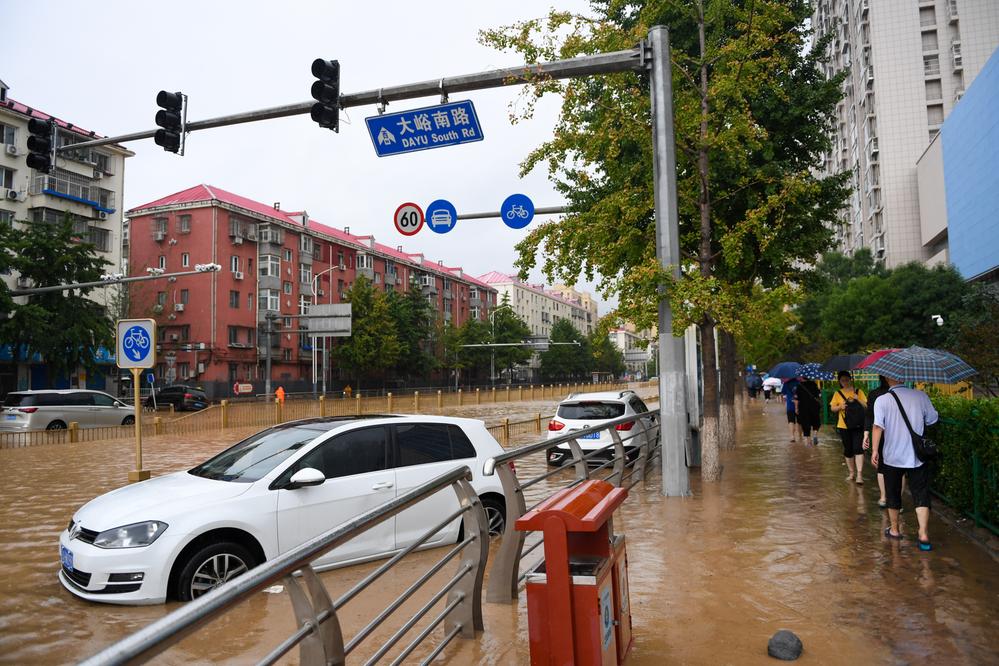 7月31日，在北京市门头沟区大峪南路，行人从积水的路面和泡水的车辆旁走过。新华社记者 鞠焕宗 摄