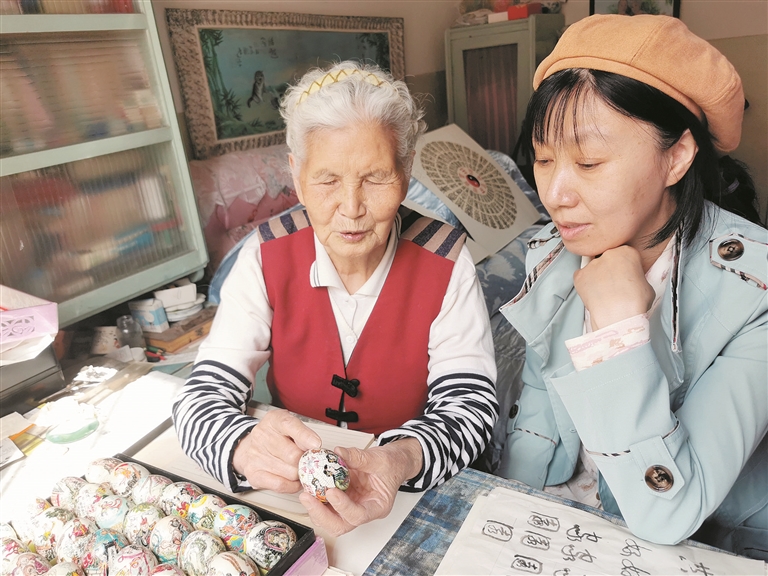 4月18日，党广云（左）向胡彩萍讲解蛋壳画制作技巧。 蒲子璇 摄