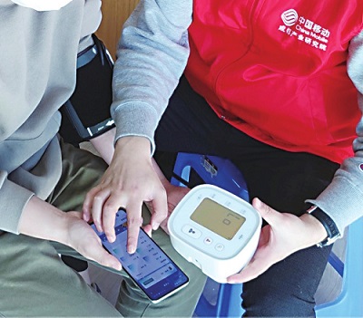 中国移动工作人员指导居民使用智能测血压功能。