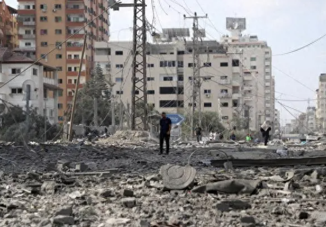 ▲10月10日，在加沙城，人们走过被以色列空袭炸毁的建筑废墟。图源：新华社