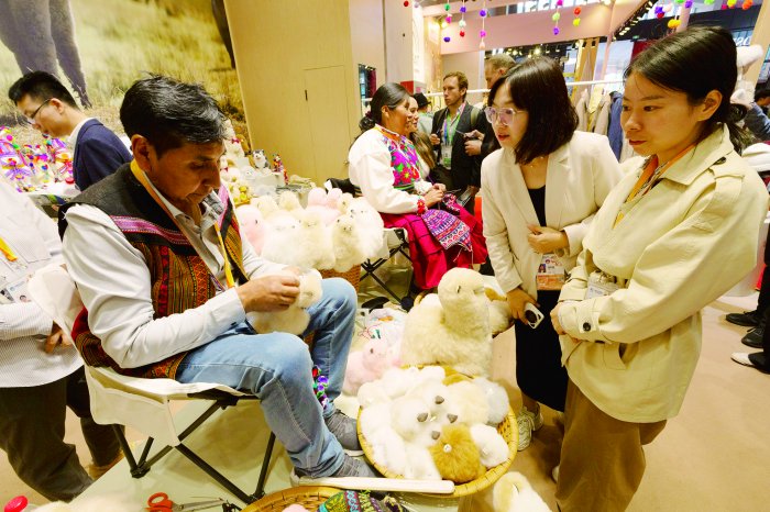 参观者在上海进博会“温暖驼”品牌展台观看秘鲁“羊驼大叔”马马尼制作羊驼玩偶 新华社图